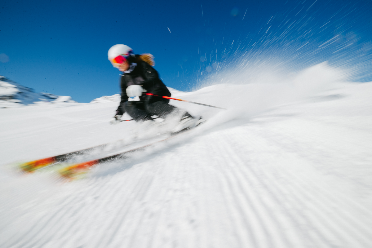 Woman in a white helmet and dark jacket skiing fast down a groomer