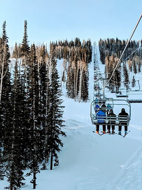 ski lift at Park City Mountain Resort with people riding up the chair in rental ski jacket and snowpants