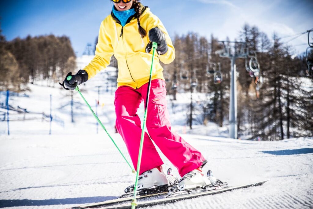 A brightly dressed woman smiling as she skis down a gentle slope on sport ski rentals in Park City, Utah